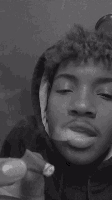 a young man is smoking a cigarette and blowing smoke out of his mouth in a black and white photo .