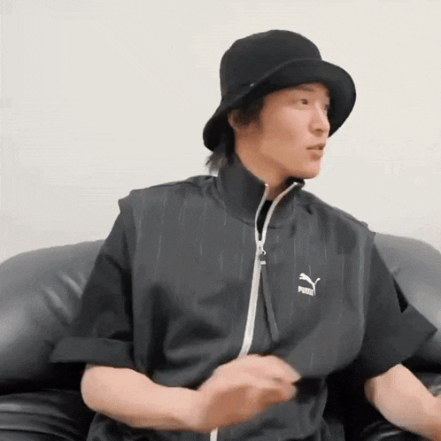 a man wearing a black hat and a black puma vest is sitting on a couch .