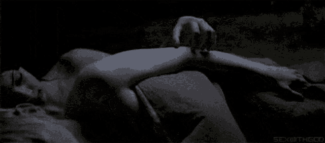 a woman is laying on a couch with a hand reaching out to touch her arm .