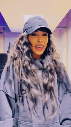 a woman wearing a hat and a hoodie is smiling