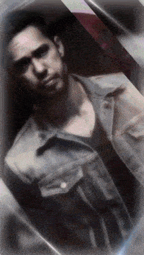 a man in a denim jacket and black shirt is looking at the camera