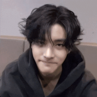 a young man with black hair is wearing a black hoodie and making a face .