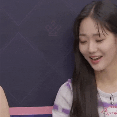 a girl with long black hair is smiling and wearing a purple shirt with a crown on it