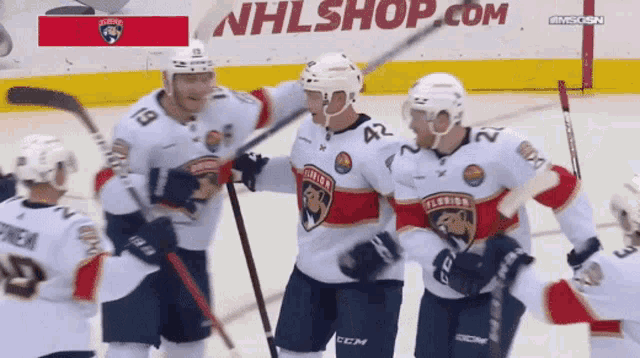 a hockey team celebrates a goal in front of an nhlshop.com banner
