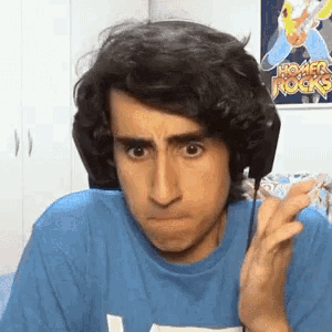 a man wearing headphones and a blue shirt is making a funny face while looking at the camera .