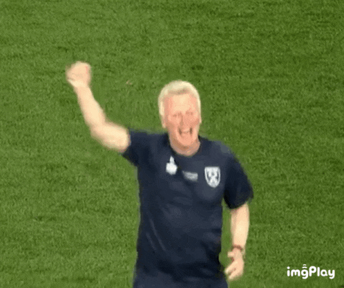 a man in a blue shirt is standing on a field with his fist in the air .