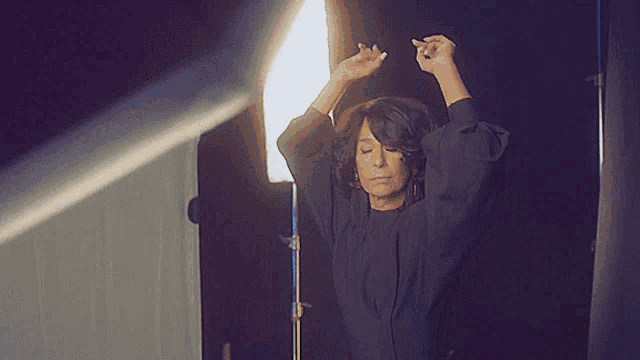 a woman in a black dress is standing in front of a light with her hands in the air