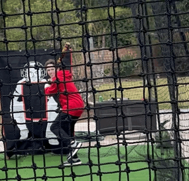 a man in a red shirt is throwing a baseball in a cage