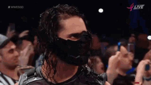 a wrestler wearing a mask is standing in front of a crowd of people .