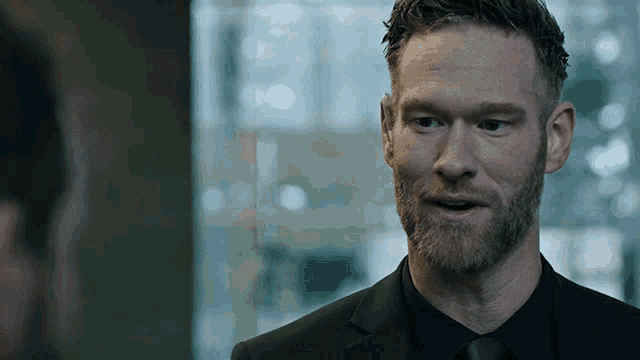 a man with a beard is wearing a black suit
