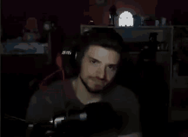 a man wearing headphones and a microphone is sitting in front of a microphone in a dark room .