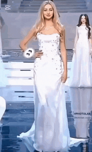 a woman in a white dress is walking down the runway at a pageant .
