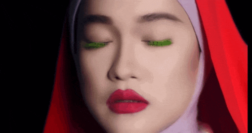 a close up of a woman 's face wearing a red veil and a hijab with her eyes closed .