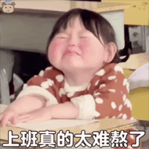 a little girl is sitting at a desk with her eyes closed and making a face .