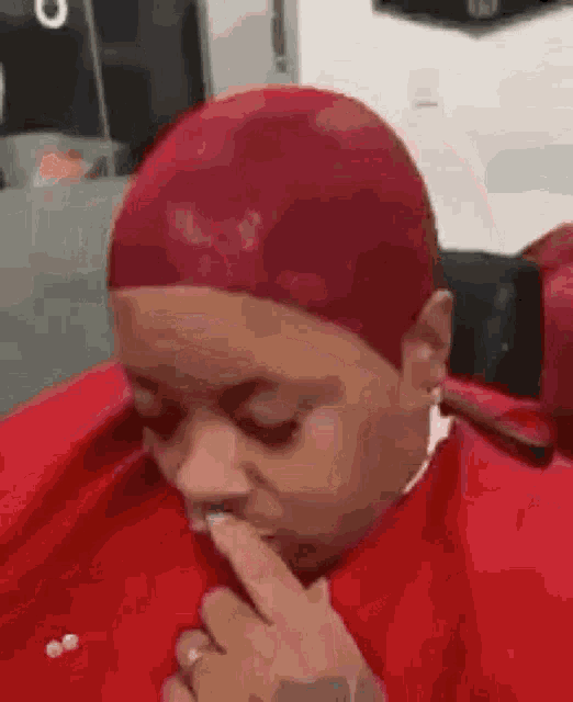 a woman with red hair is sitting in a red cape and covering her mouth with her hand .