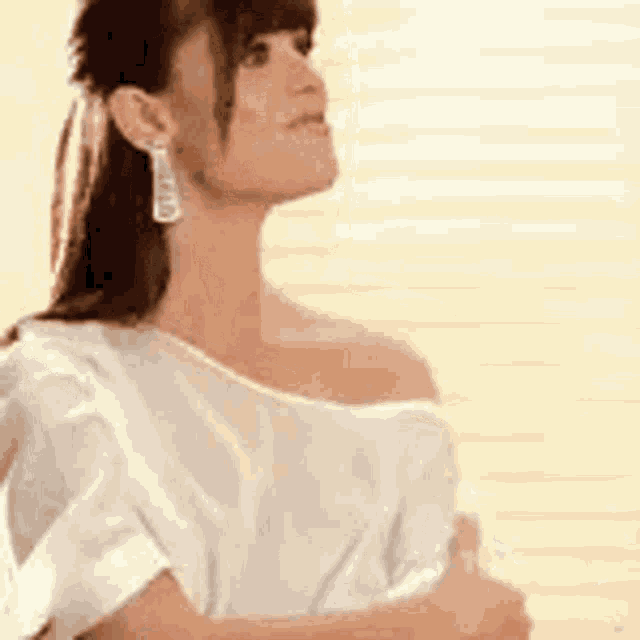 a woman wearing a white off the shoulder top and earrings .