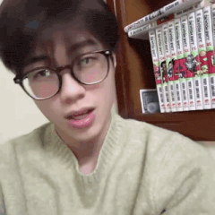 a young man wearing glasses is standing in front of a bookshelf .