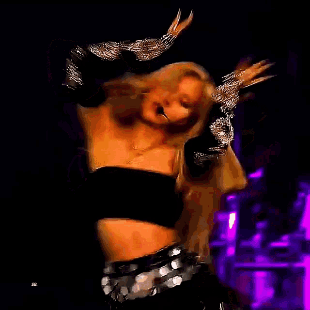 a woman in a black crop top and sequined skirt is dancing on stage .