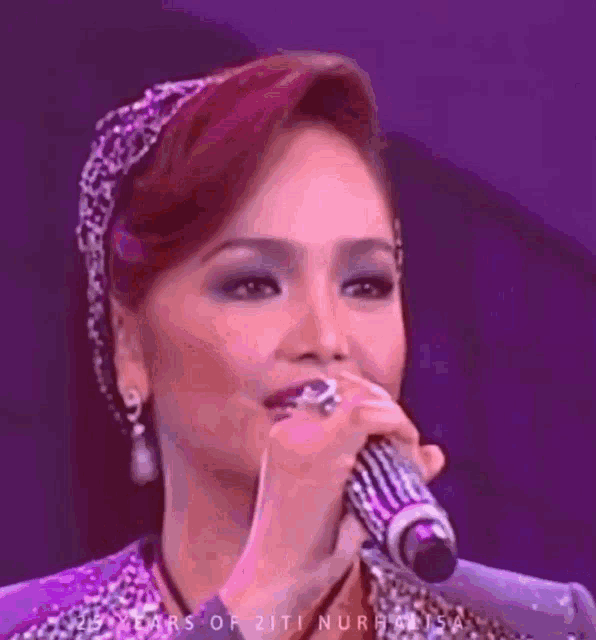 a woman is singing into a microphone with a purple background .