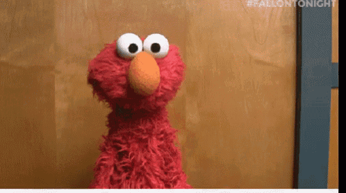 elmo from sesame street is standing in front of a wooden door and looking at the camera .
