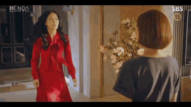 two women are standing next to each other in a room with a vase of flowers .