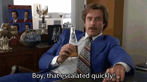 a man in a blue suit and tie is sitting at a desk holding a beer and says boy that escalated quickly