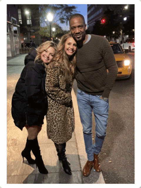three people posing for a picture on a sidewalk with a taxi in the background