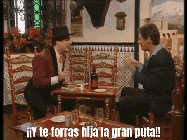 two men sitting at a table with the words " y te forras hija la gran puta " written on the table