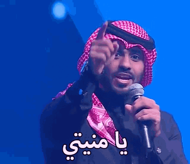 a man wearing a keffiyeh is holding a microphone and pointing