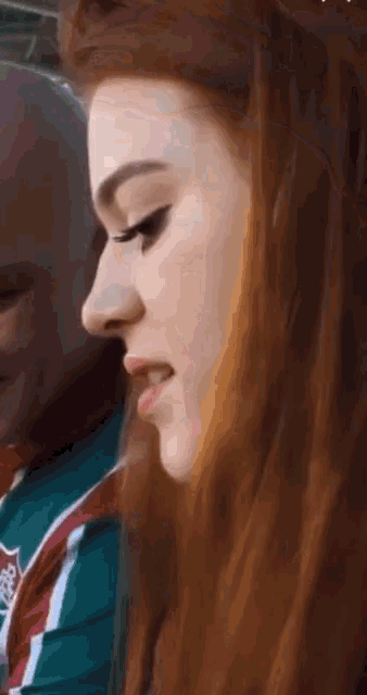 a close up of a woman 's face with red hair and a man 's face in the background .