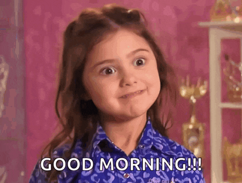 a little girl is wearing a blue shirt and making a face and saying good morning .