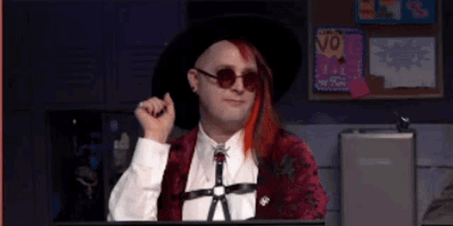 a man with red hair and sunglasses is sitting in front of a computer screen .