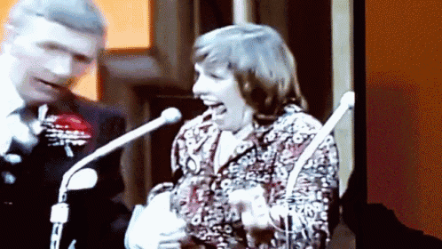 a man and a woman are standing in front of microphones and the woman is laughing