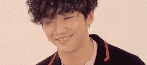 a young man with curly hair is smiling and wearing a black jacket and earrings .