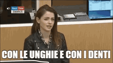 a woman in a leather jacket is sitting in front of a computer and says con le unghie con i denti .