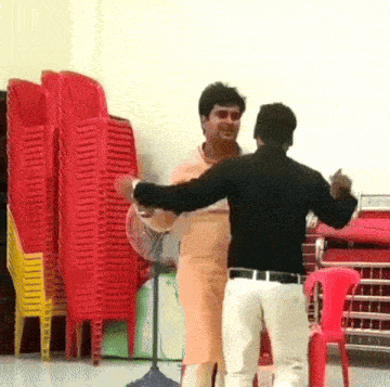 two men are dancing in a room with red chairs