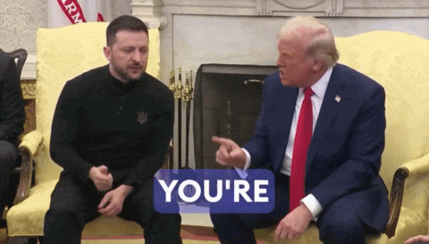 two men are sitting on a couch and one has a sign that says you 're