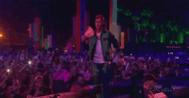 a man in a green jacket stands on a stage in front of a crowd with the words coachella on the bottom right