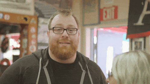 a man with glasses and a beard is standing in front of an exit sign