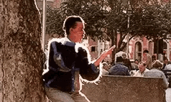 a man is leaning against a tree while looking at his cell phone .