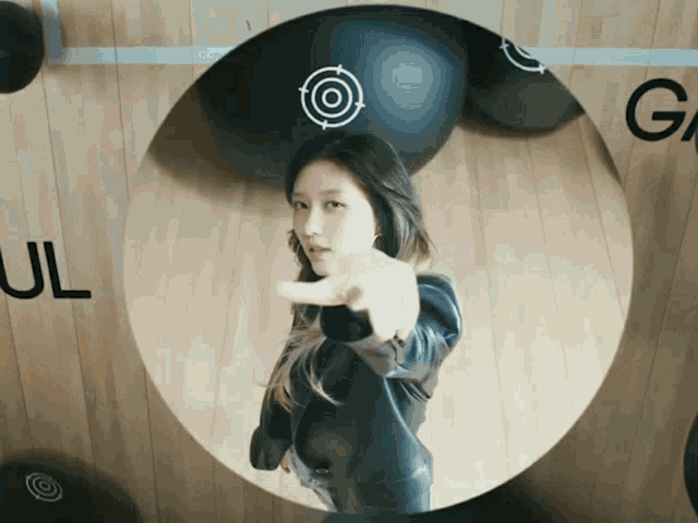a woman is pointing at the camera in front of a target with the letter g on it