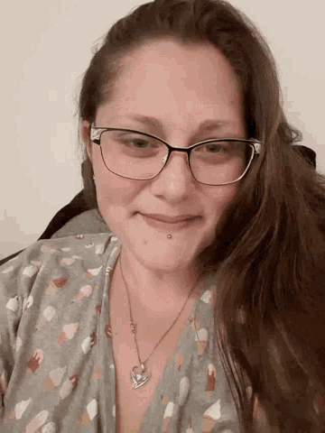 a woman wearing glasses and a necklace smiles for the camera