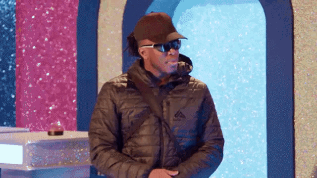 a man wearing a hat and sunglasses is standing in front of a pink and blue wall