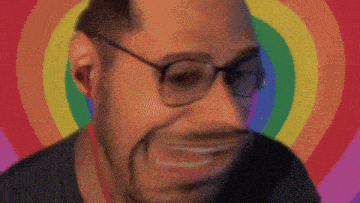 a man wearing glasses and ear buds is smiling in front of a rainbow background