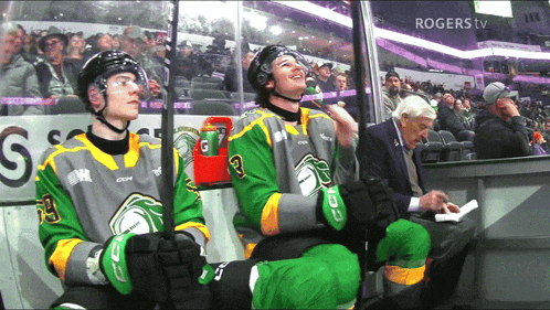 two hockey players are sitting in the stands with rogers tv in the corner