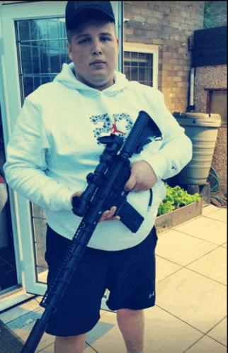 a man wearing a white hoodie with the number 33 on it holds a gun