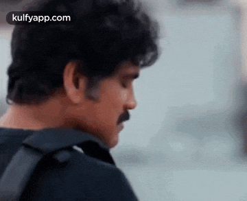 a man with a mustache and a backpack is looking down at something .