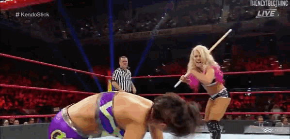 two women are wrestling in a ring with a referee watching