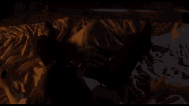 a man in a white shirt is laying on a bed in a dark room with his mouth open .