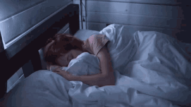 a woman is sleeping on a bed with white sheets